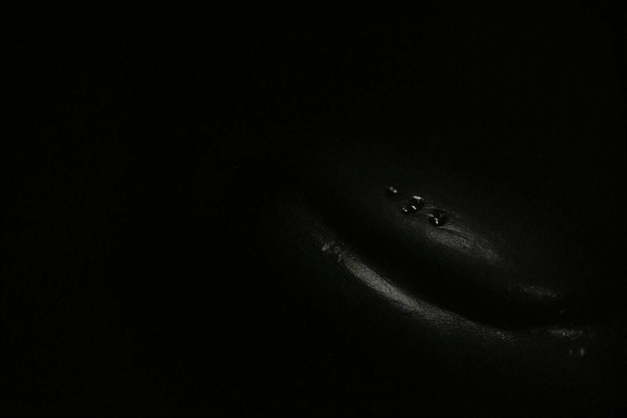 An almost entirely black photograph. A faint sheen along one curve and three small reflective glints are the only things visible.