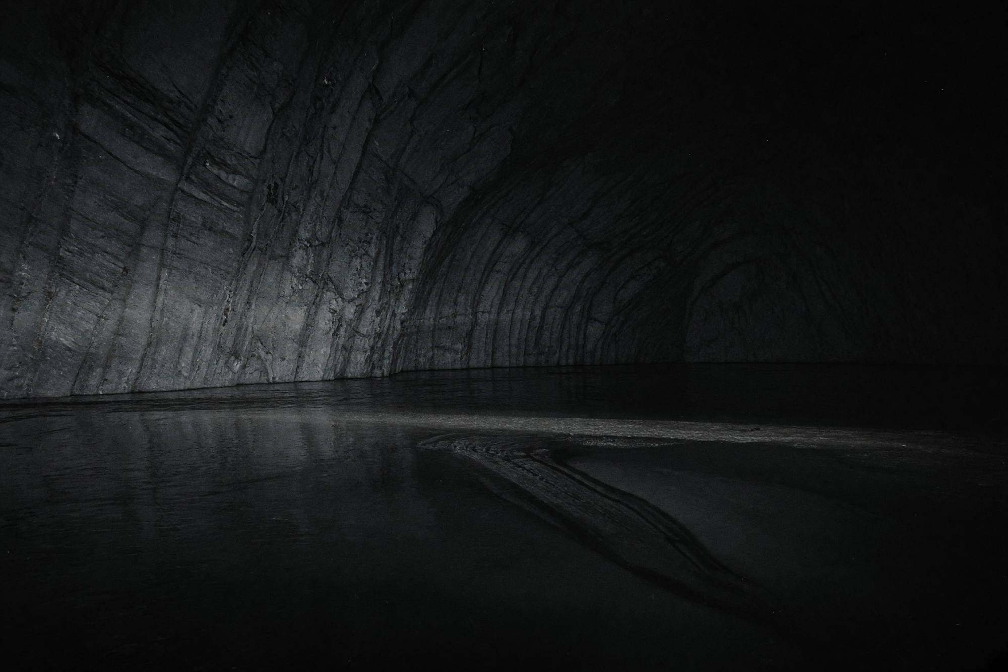 A vast dark ice cavern lit by a single weak lamp, with still black water along the floor.